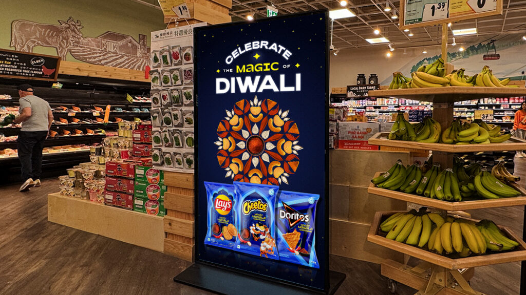 Digital Diwali celebration signage with Lay’s, Cheetos, and Doritos display inside a grocery store produce aisle.
